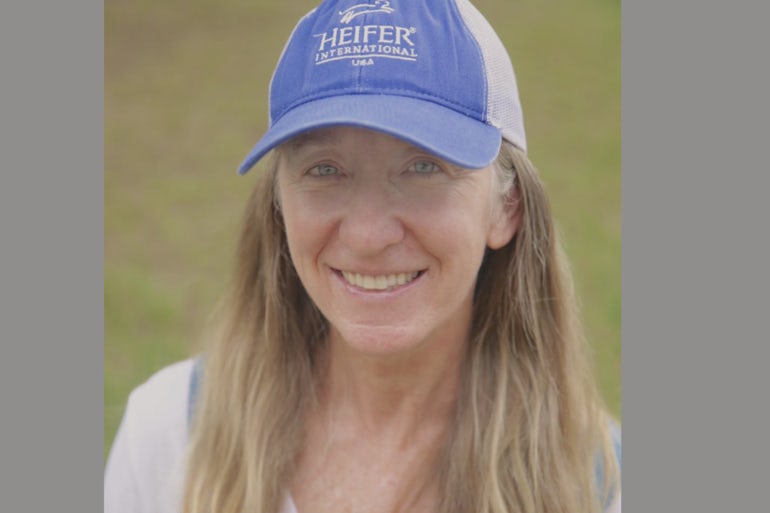 A woman wearing a blue Heifer hat smiles at the camera.