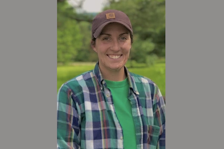 A woman wearing a checkered shirt and brown baseball cap smiles at the camera.