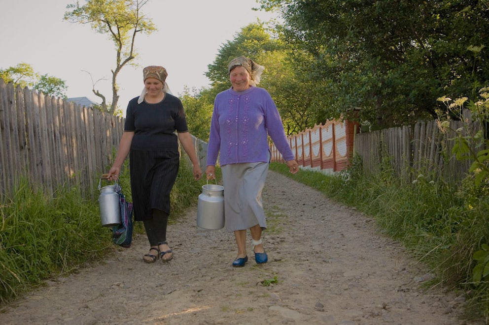 Two women carry canisters of milk in Ukraine.