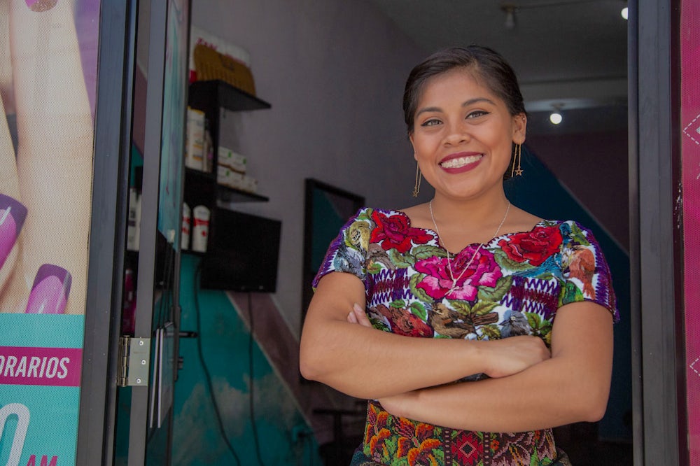 A woman stands in the doorway of her salon business with a smile.