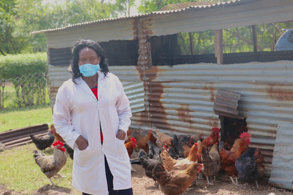 A Kenyan woman stands for a portrait at her home poultry farm.
