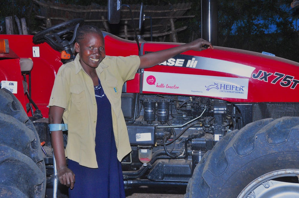 A woman stands in front of her tractor.