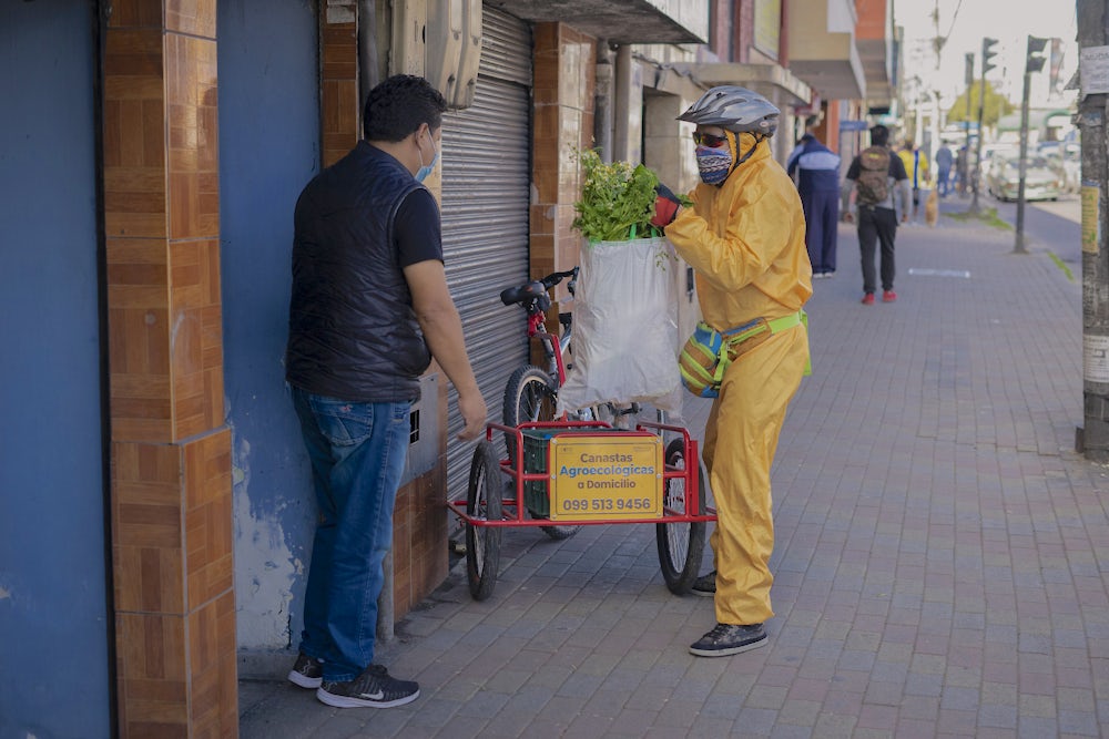 A man in protective gear hands a basket of food to another man.