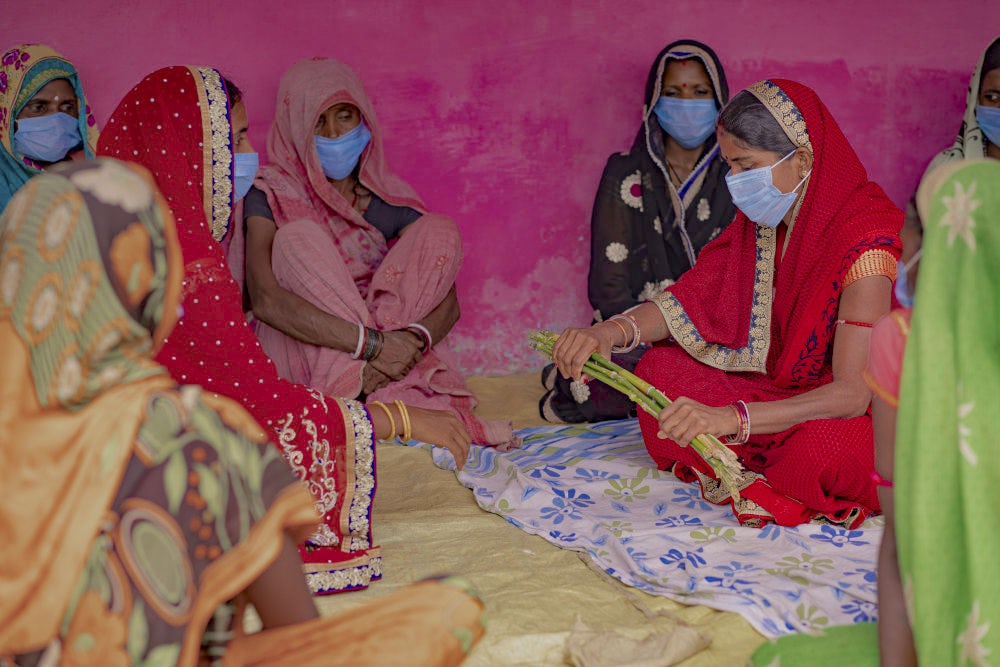 A group of women sitting in a circle and conducting an activity with sticks to explain the strength of collective. 