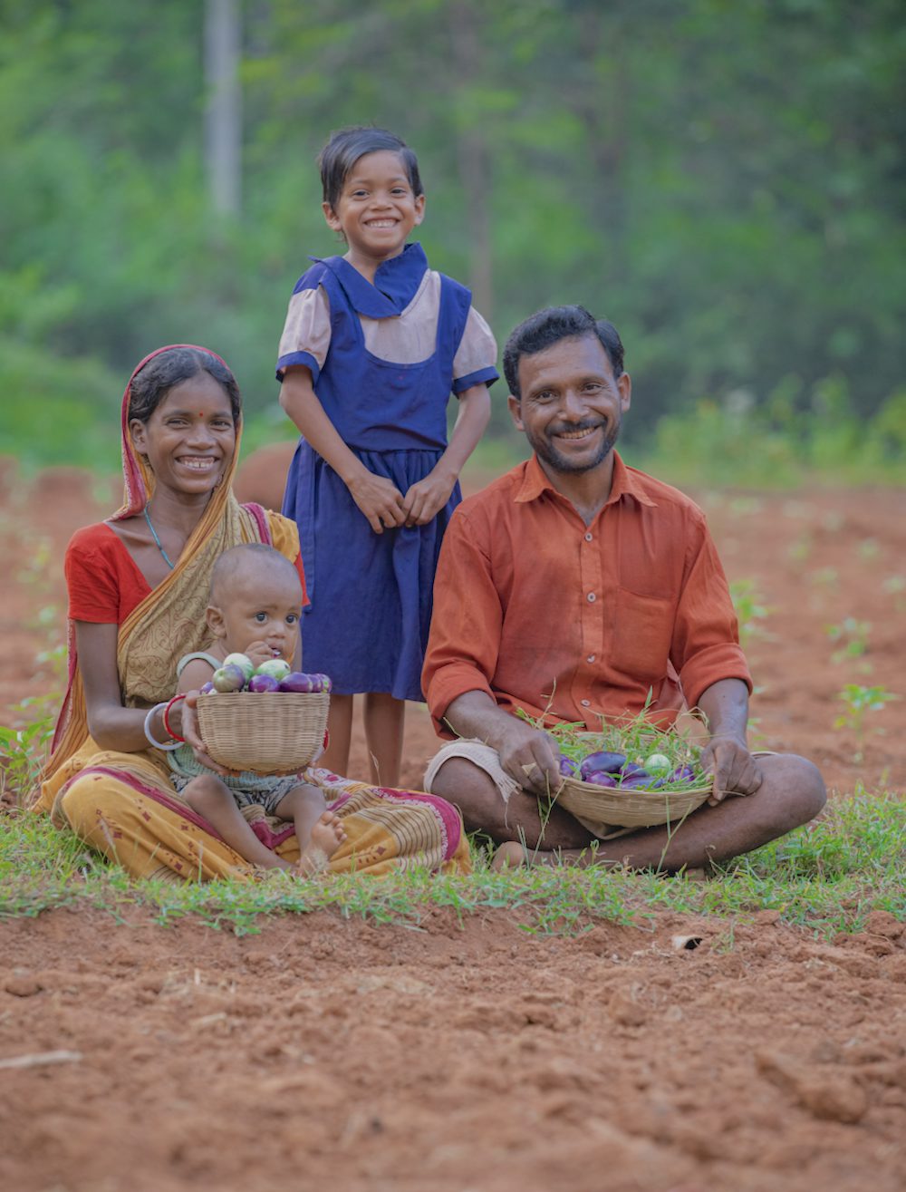 A mother, father and two young children sit together in a field in India.