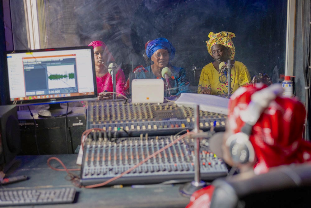 Three women speak into microphones in a radio recording station.