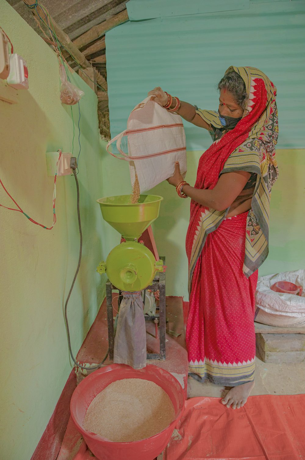A woman pours chicken feed into a small mill.