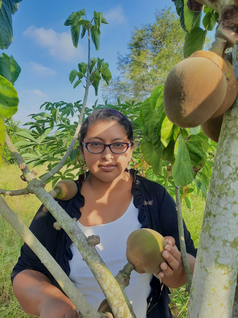 A woman stands next to a fruit tree in Ecuador.