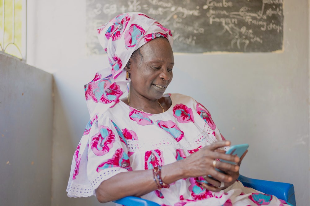 A Senegalese women sits on a chair and looks at her mobile phone.