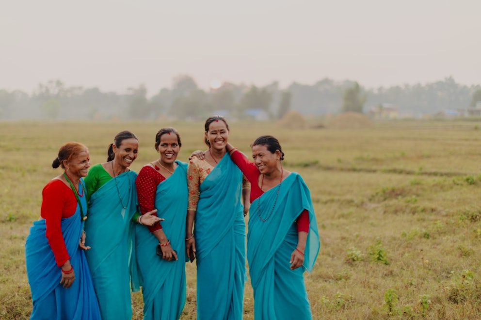 Five women laugh together in a field in Nepal.
