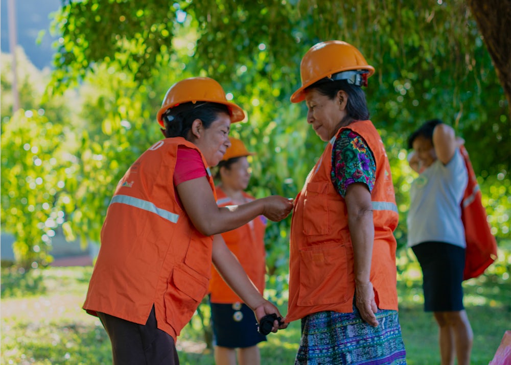 A woman zips up the vest of another woman in a Guatemalan forest.