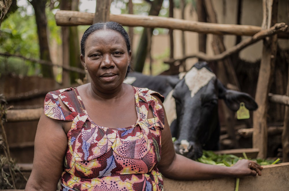 A woman in Rwanda stands in front of her family's cow.