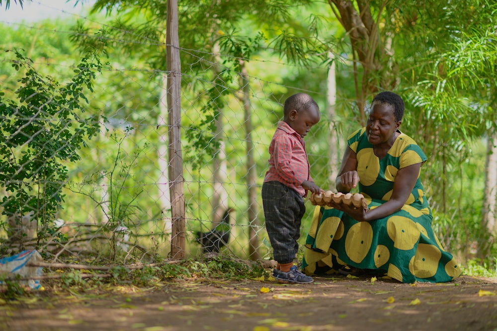 A woman in Kenya holds a carton of eggs out towards a small boy.