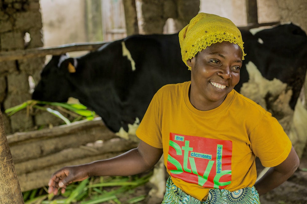 A woman dairy farmer in Rwanda smiling in front of her cow shed.