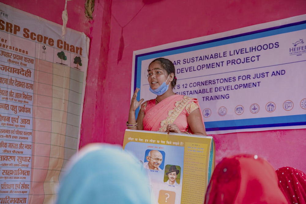 A woman holding a learning guide and addressing a group of women during a training session. 
