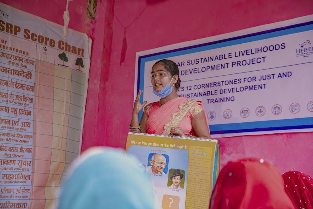 A woman holding a learning guide and addressing a group of women during a training session.