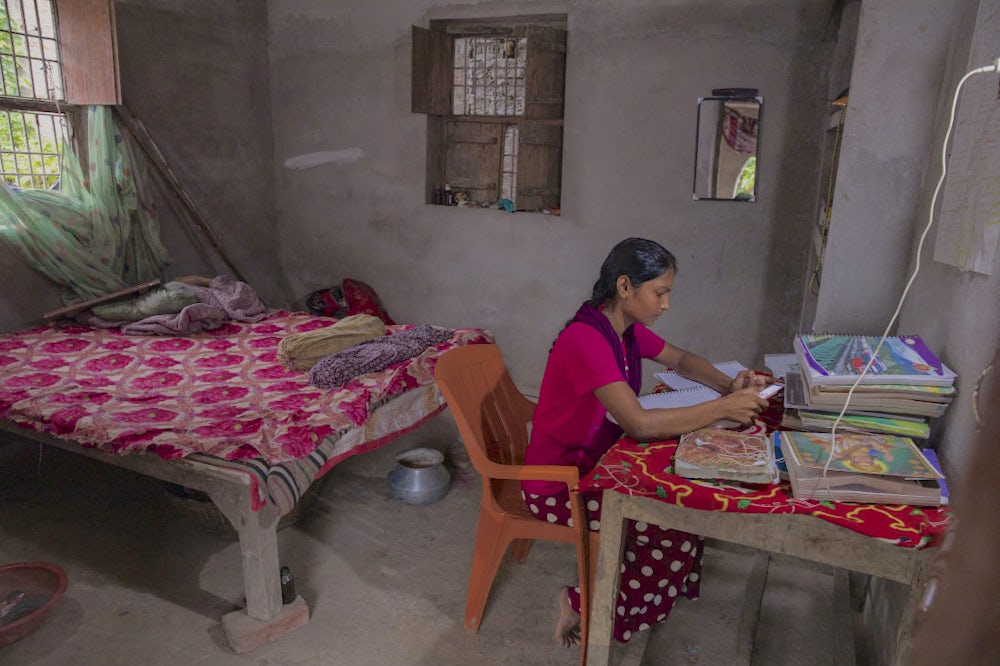 A girl sitting in a room and studying from her books and mobile phone. 