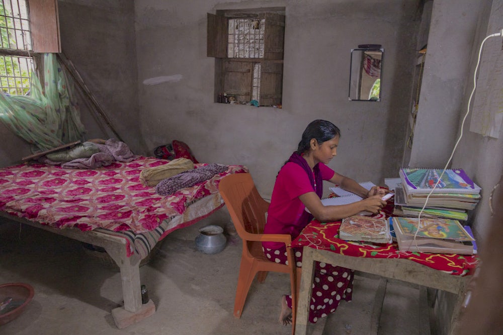 A girl sitting in a room and studying from her books and mobile phone.
