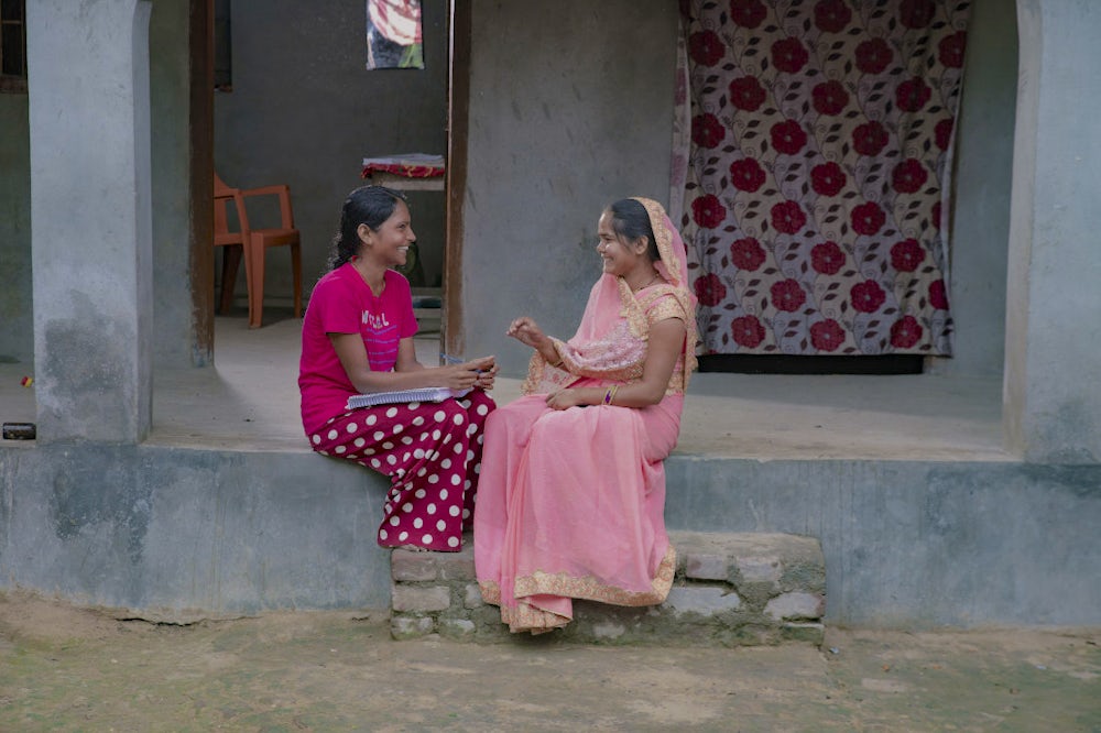 A woman and a young girl sitting together on a patio outside a house in a village.