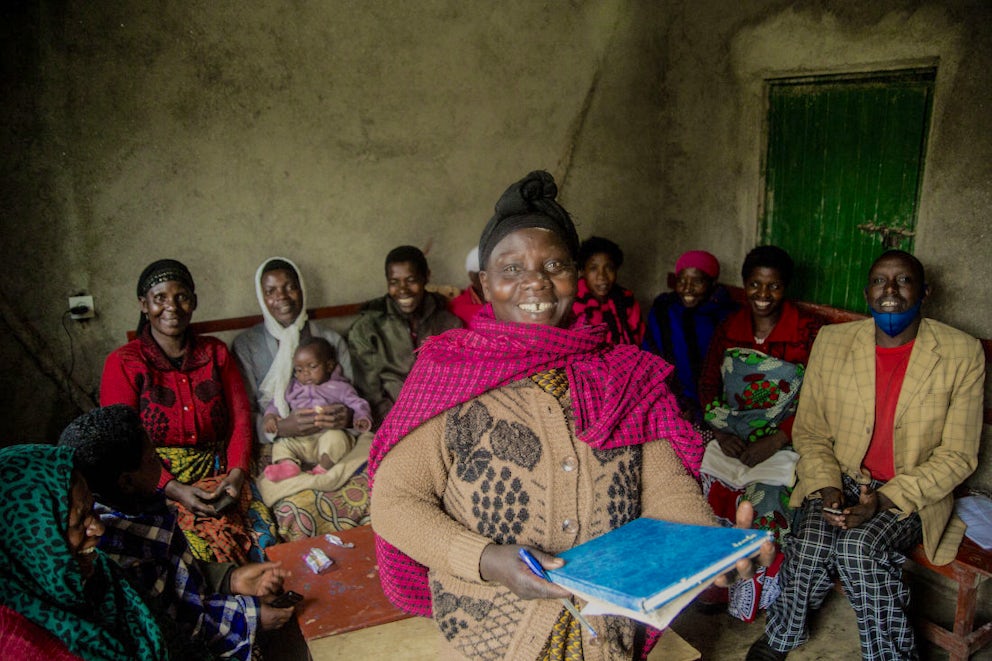 A woman holding a record keeping diary and standing with the members of her self-help group.