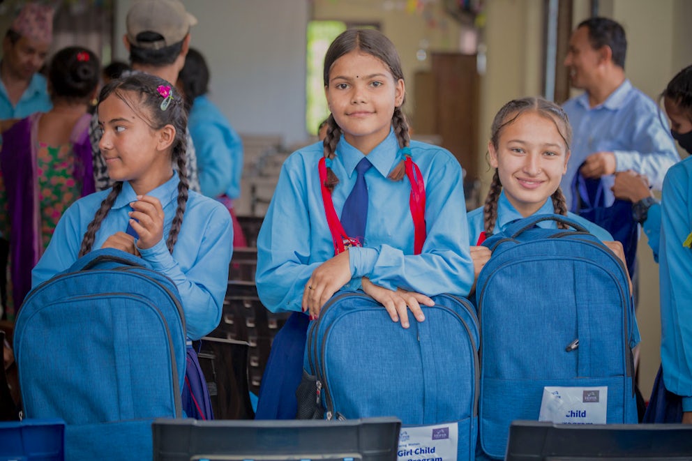 Three girls sit together holding new backpacks in Nepal.