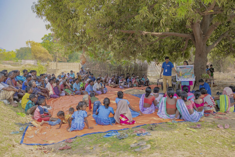 A community trainer delivering a session on poultry production practices to a group of men and women in a village. 