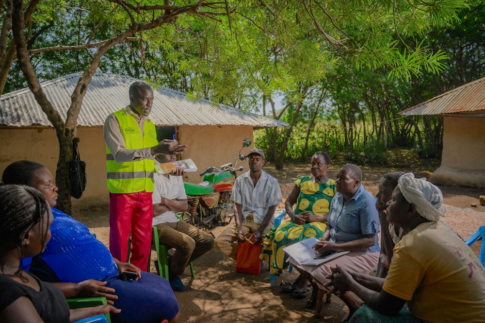 一名男子向一群男人和女人讲话，并在一个村庄的地面上进行培训。