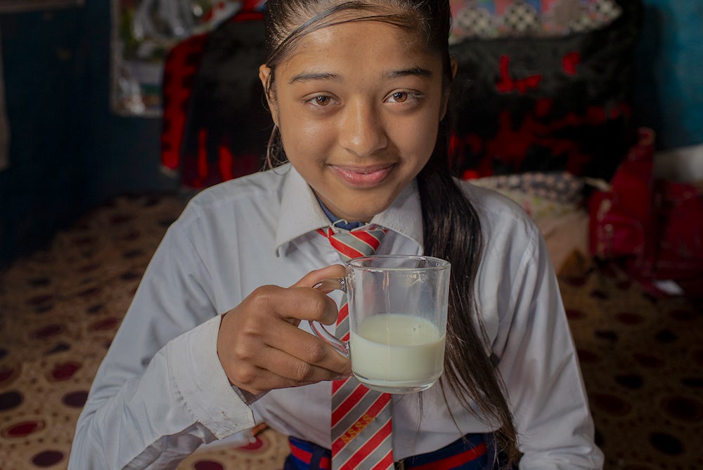 A young girl sips a glass of milk.