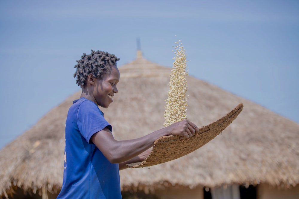 A woman smiles while tossing soybean seeds on a tray.
