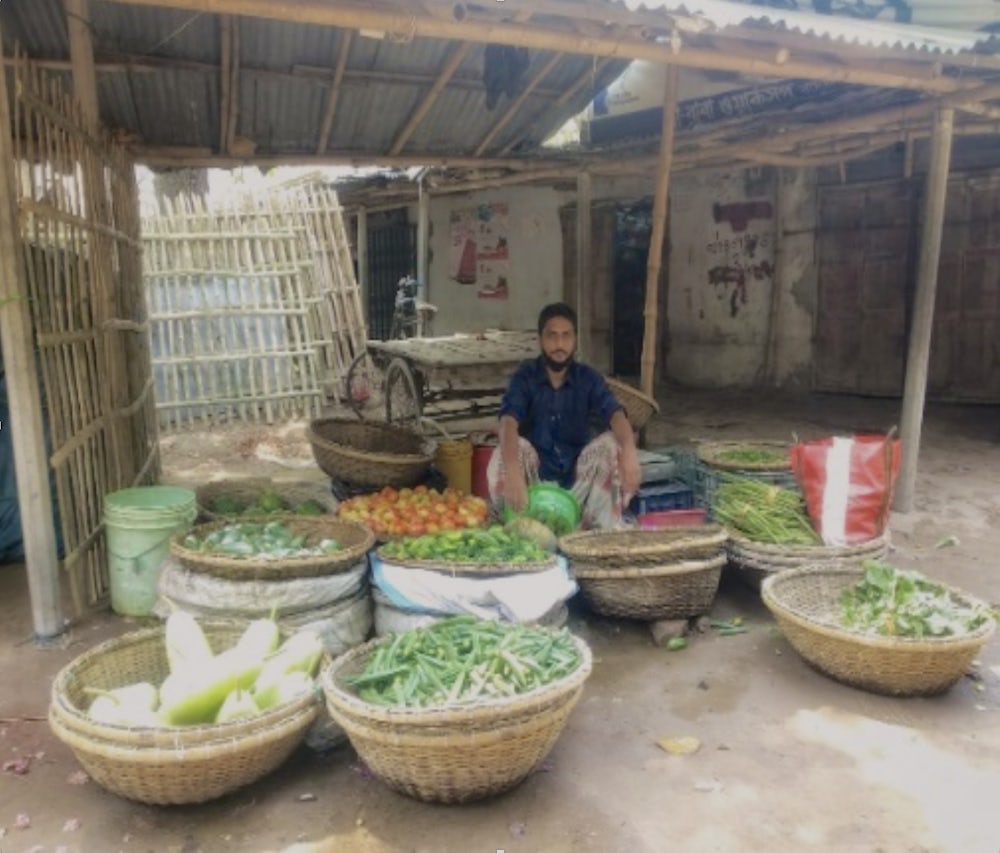 A man sits in a vegetable stall in Bangladesh, waiting for customers.
