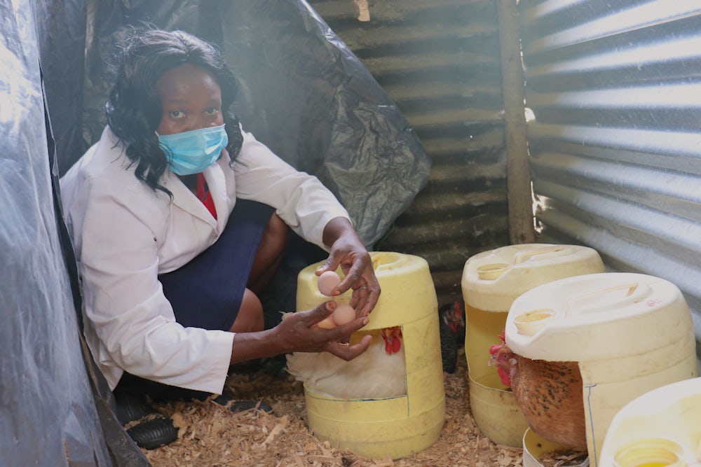 A Kenyan chicken farmer crouches by her chickens in their laying pots and collects their eggs.