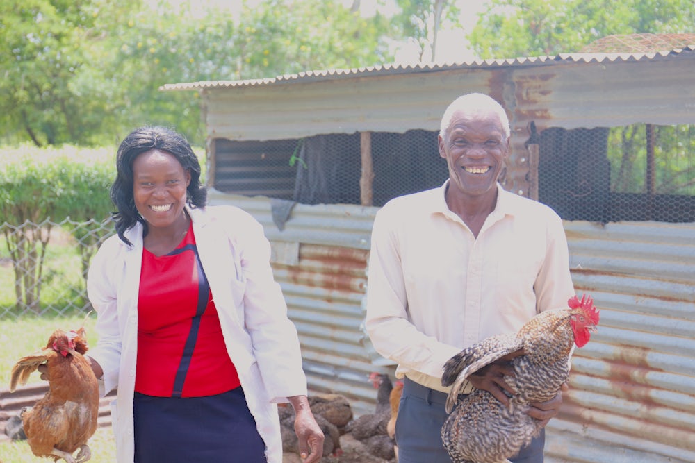 A Kenyan woman stands next to her dad in front of their thriving chicken coop.