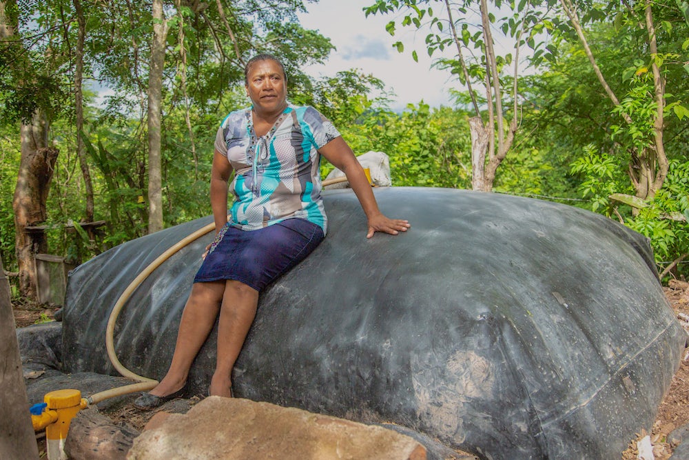 A Nicaraguan woman leans against a big grey dome in her backyard. The dome is a biogas unit.