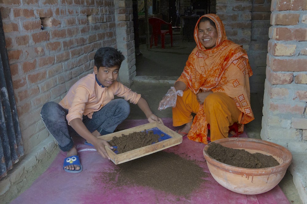 A woman and her nephew crouch next to a bowl full of vermicompost.