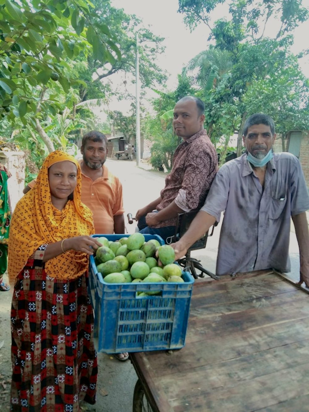 A woman poses for a photo with her mangoes alongside three men who will transport the mangoes.