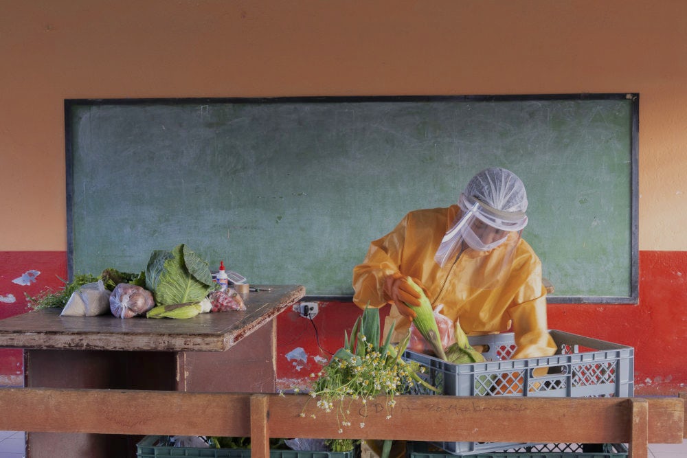 A man wearing a personal protective equipment and face mask is sorting vegetables on a table. 