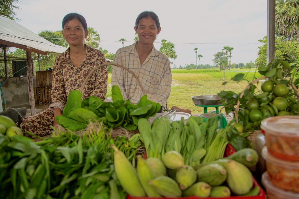 Two women standing behind a bunch of colorful vegetables.