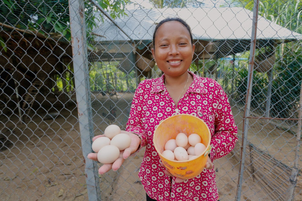 A woman holds eggs and smiles for the camera.