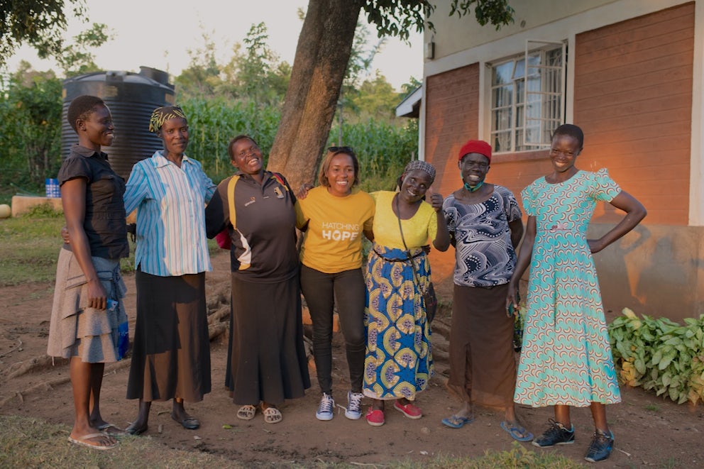 Seven Kenyan woman stand arm-in-arm, smiling and facing the camera.