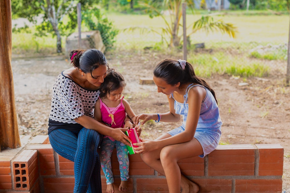 Digna Silva and her two daughters sit on a low brick wall, reading a book together.