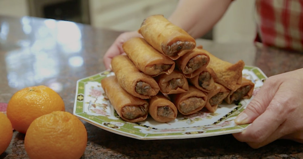 Spring Rolls on a white and green china plate next to oranges.