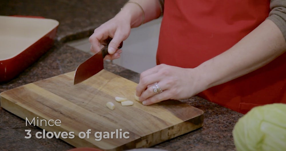 A demonstration shot of mincing garlic - one hand holds a kitchen knife and one holds cloves of garlic. 