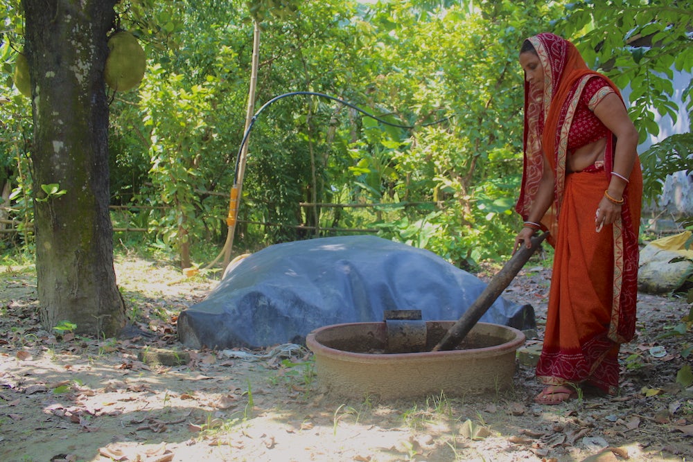 An Indian woman mixes a big wooden pot in her yard.
