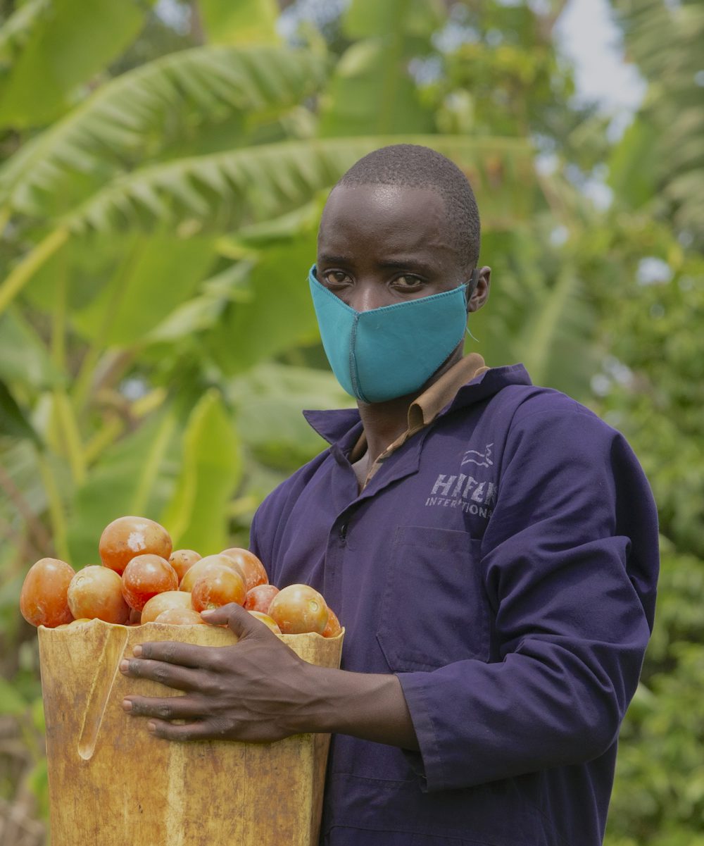 A young Ugandan man holds a basket of his tomatoes.