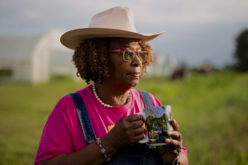 A woman wearing a hat and holding a coffee cup in her hands, stares into the distance.