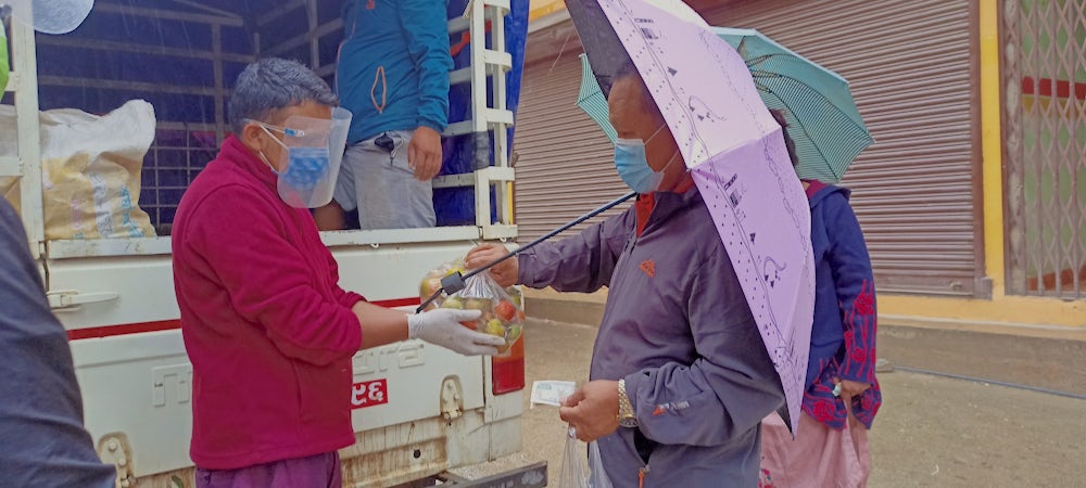 A community member exchanges money for a bundle of vegetables.