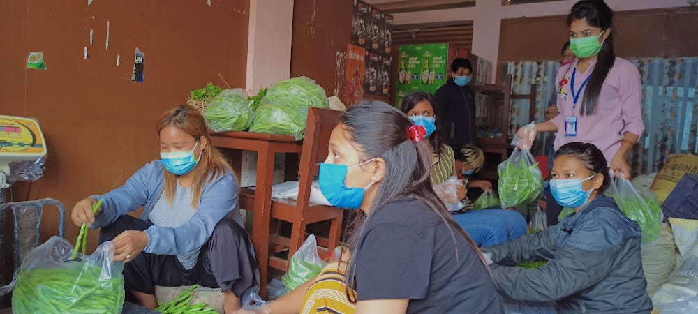 Six women package and weight bags of fresh vegetables.