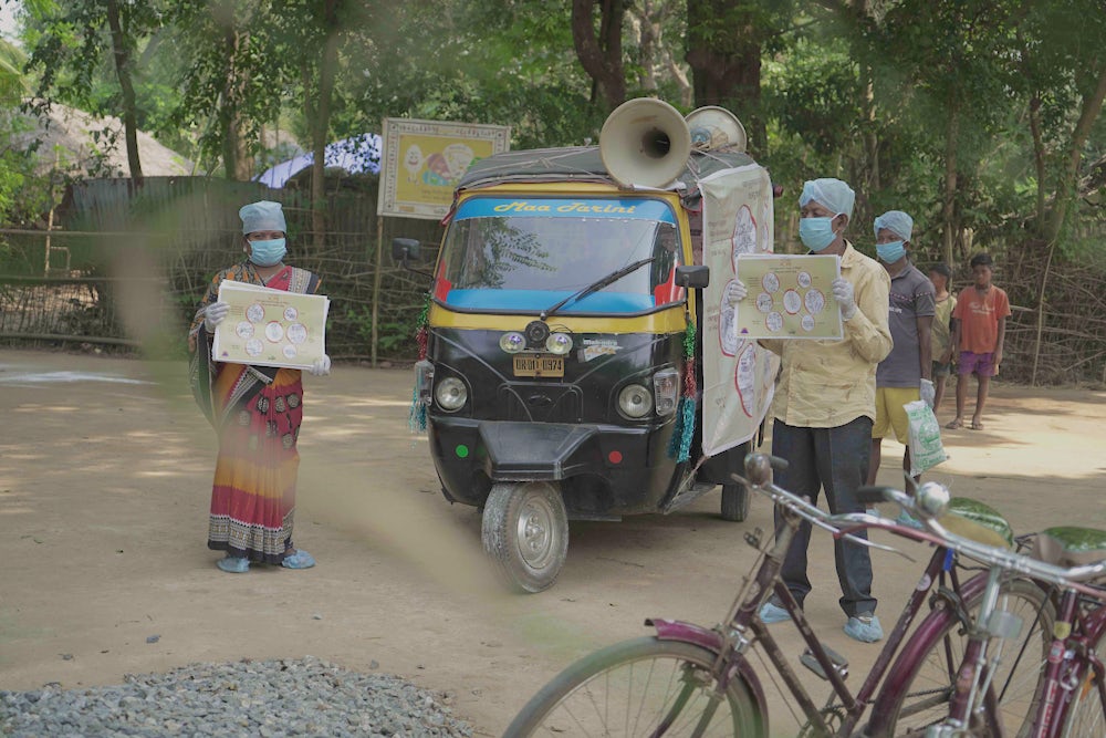 Two masked health workers hold signs promoting biosecurity measures.