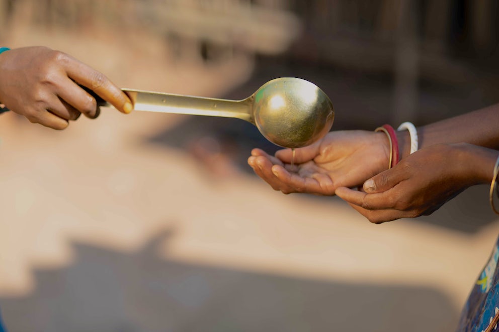 A ladle pours an orange disinfectant liquid into a pair of hands.