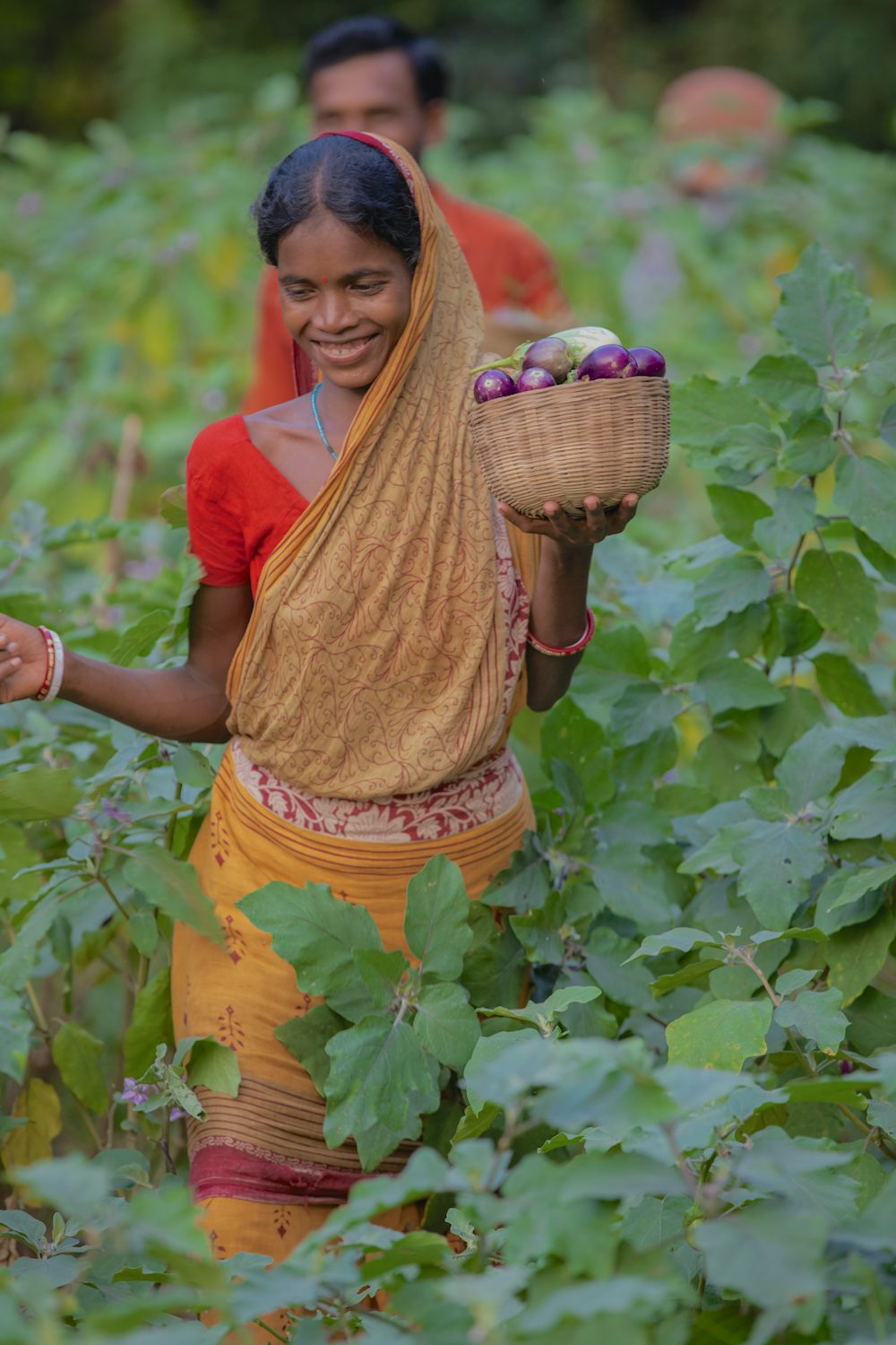 A smiling woman in India walks through her vegetable field.